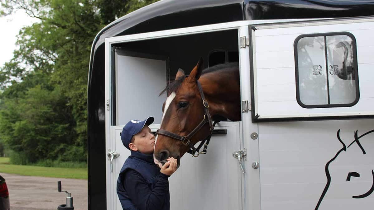 Un cavallo sporge la testa da un furgone. Un ragazzo lo bacia sul naso.