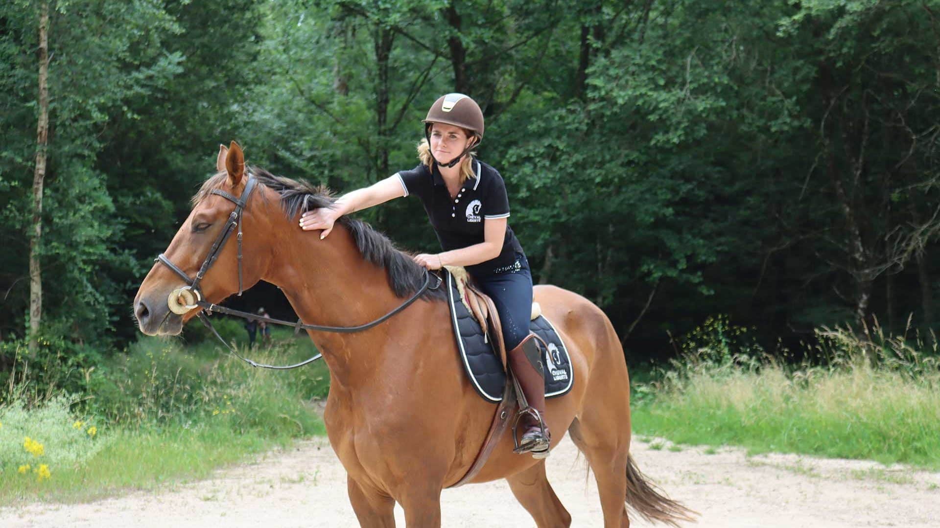 Una cavallerizza ferma accarezza il suo cavallo nella foresta, sorridendo.